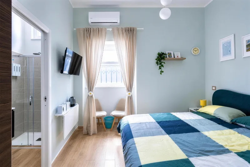 Camera doppia con pareti azzurro polvere, letto matrimoniale e tende color sabbia